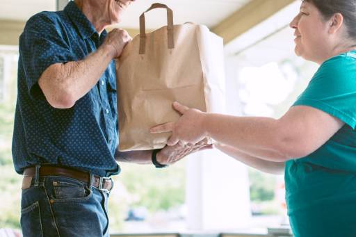 Senior man being handed a bag of groceries by a woman