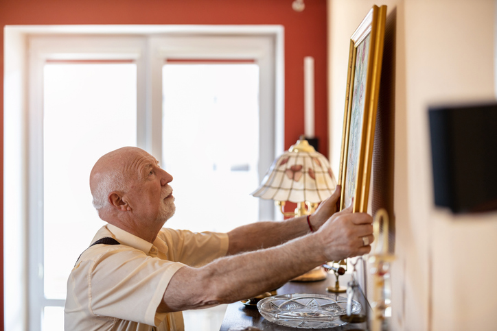 Senior man hanging a painting on a wall.